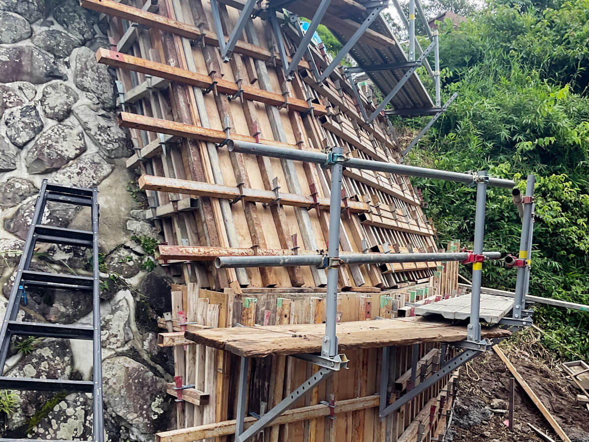 石積みの法面で、木製型枠と足場が組まれた擁壁工事の施工状況